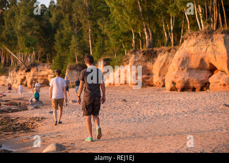 Les jeunes hommes sont à pied à côté de grottes calcaires et de falaises sur la plage pendant le coucher du soleil chaud et lumineux. Soirée romantique dans la nature. Concept d'une saine et activ Banque D'Images