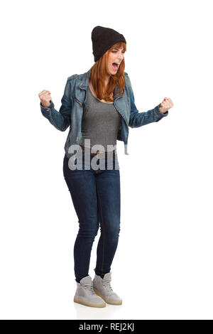 Jeune femme en colère en jeans et blouson cap est debout, work et crier. Studio pleine longueur shot isolé sur blanc. Banque D'Images