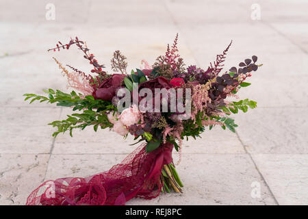 Bouquet de mariage rouge sombre se dresse sur fond de murs en pierre Banque D'Images