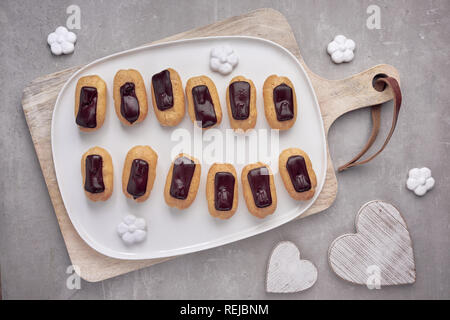 Mini éclairs vanille glaçage au chocolat sur fond noir en lumière, vue du dessus Banque D'Images