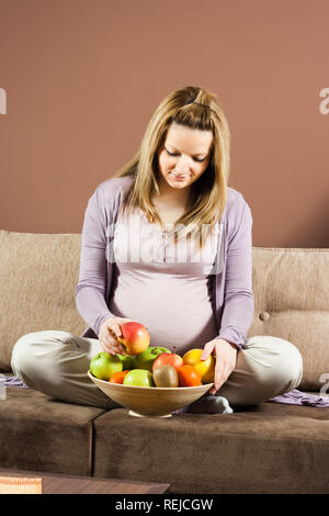 Pregnant woman sitting on sofa avec bol plein de fruits Banque D'Images