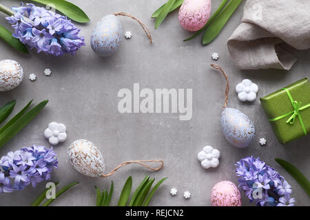 Mise à plat de Pâques avec les oeufs de Pâques, jacinthe bleu et fleurs en céramique blanche sur fond noir en lumière Banque D'Images