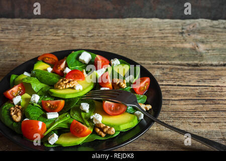 L'avocat et salade d'épinards avec des tomates cerise, de la feta et les noix dans une assiette sur une table en bois rustique. alimentation saine. close up Banque D'Images