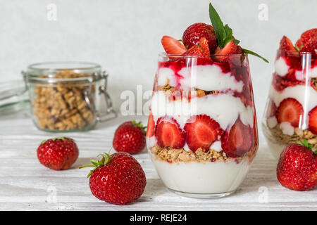 Du yaourt fait maison parfait glacé à la fraise au granola et verres sur table en bois blanc, petit-déjeuner sain. Banque D'Images