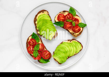 L'avocat et d'hummus et toasts tomates basilic dans une plaque sur fond de marbre blanc. La nourriture végane. Vue de dessus Banque D'Images