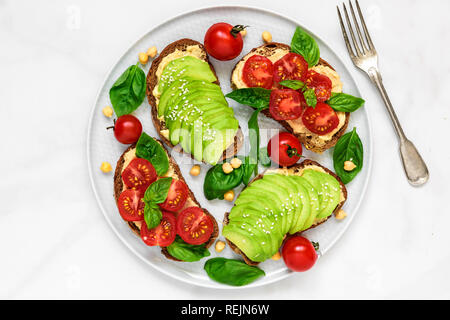 L'avocat et les tomates sandwiches sains d'hummus, sésame et basilic dans une assiette avec une fourchette sur fond de marbre blanc. La nourriture végane. Vue de dessus Banque D'Images