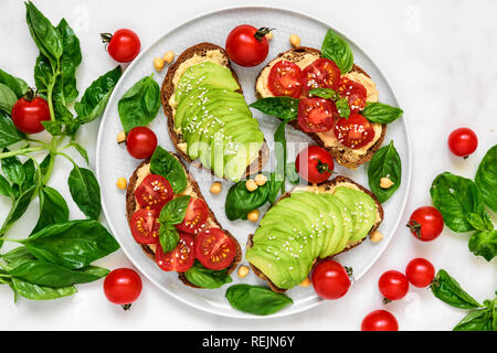 L'avocat et les tomates toasts avec du hoummos, sésame et basilic dans une plaque sur fond de marbre blanc. La nourriture végane. Vue de dessus Banque D'Images