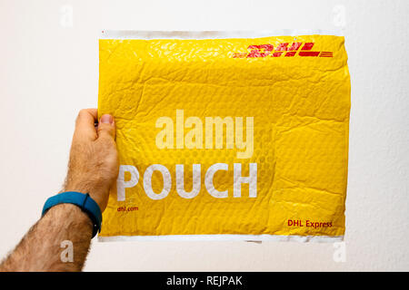 Francfort, Allemagne - MAR 24, 2018 : Close-up of man holding colis DHL Express jaune pouch against white background Banque D'Images