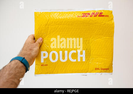 Francfort, Allemagne - MAR 24, 2018 : smartwatch holding colis DHL Express jaune pouch against white background Banque D'Images