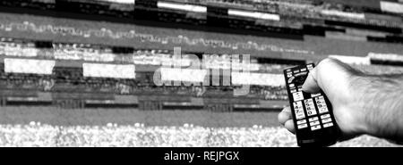 Homme avec grande télévision à essayer de réparer à distance le bruit de la télévision numérique sur un grand écran OLED plasma 4K Ultra HD HDR High Dynamic Range - Smart TV noir et blanc. Banque D'Images