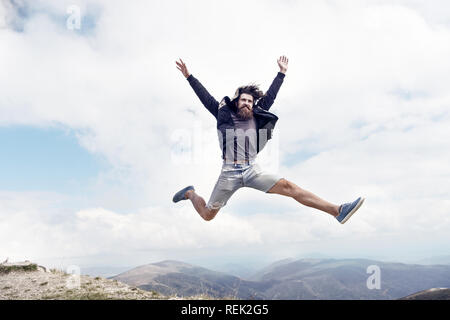 Homme barbu, longue barbe, brutal caucasian hipster avec moustache saut avec un visage heureux en montagne avec ciel nuageux, guy non rasé avec des cheveux ne coupe de barbe sur fond naturel Banque D'Images