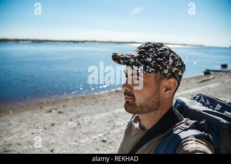 Bel homme qu'avec sac à dos à la recherche de belle rivière de chaude journée d'été. Banque D'Images