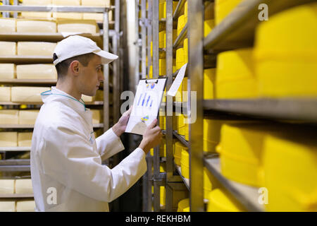 Homme avec un graphique dans sa main vérifie les statistiques dans l'entrepôt de fromage Banque D'Images