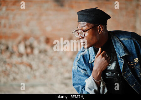 African American man veste en jeans, béret et lunettes à la briqueterie abandonnée. Banque D'Images