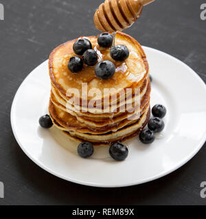 Pancakes aux myrtilles et du miel sur une plaque ronde blanche sur fond noir foncé, vue de côté. Close-up. Banque D'Images