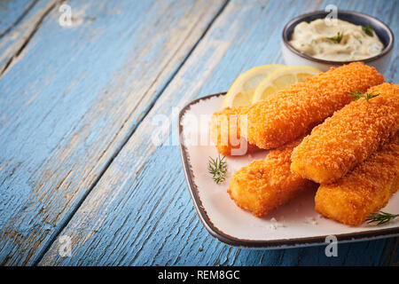 Aromatiques d'crumbed savoureux bâtonnets de poisson cuite au four pour un son net servi sur une assiette avec une sauce tartare et copiez l'espace sur bois rustique Banque D'Images