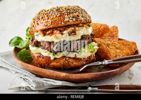 Burger de boeuf cuites avec des noix et fromage servi avec bébé épinards sur une plaque rustique et une serviette dans une vue en gros plan Banque D'Images