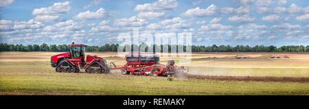 Rouge sur un fond agricole tracteur tirant la charrue, jeter la poussière dans l'air. Moissonneuse Batteuse à champ de blé. Au cours de la culture de la machinerie lourde, wor Banque D'Images