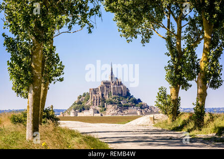 Le Mont Saint-Michel, l'île de marée en Normandie, France, vu depuis un chemin bordé de peupliers, dans les polders sous un soleil éclatant. Banque D'Images