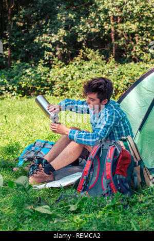 Passer un séjour sur le camping. Préparer un repas en plein air. Jeune homme prochain voyage de planification et de boire un café Banque D'Images