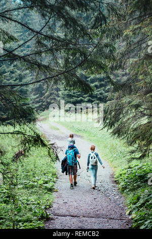 Balades en famille dans la forêt. Homme avec sac à dos, en compagnie de jeune femme, portant une petite fille sur ses épaules, marcher le long de la route forestière Banque D'Images