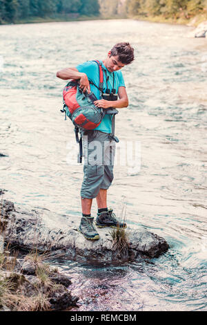 Jeune garçon prend une chope de prendre l'eau pure d'une rivière. Il est debout sur un rocher au-dessus de la rivière, se repose pendant une randonnée, passe des vacances sur wa Banque D'Images