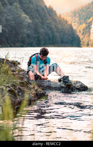 Jeune garçon prend de l'eau pure d'une rivière et la tient dans les mains. Il est assis sur un rocher au-dessus de la rivière, se repose pendant une randonnée, passe des vacances sur w Banque D'Images
