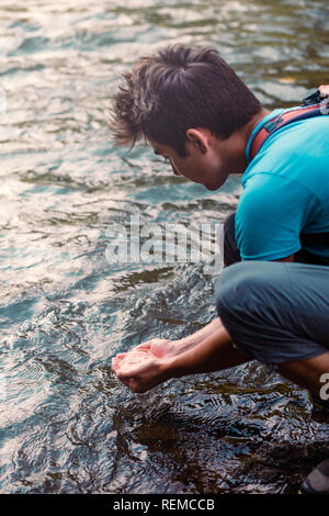 Jeune garçon en prenant l'eau pure d'une rivière et de le maintenir dans les mains Banque D'Images