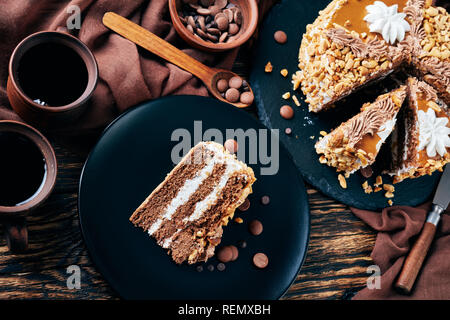 Gâteau d'arachides recouvertes de beurre d'arachide et de cacao crème oeufs roses servi sur une plaque noire sur une table en bois rustique avec du café en tasse de faïence Banque D'Images