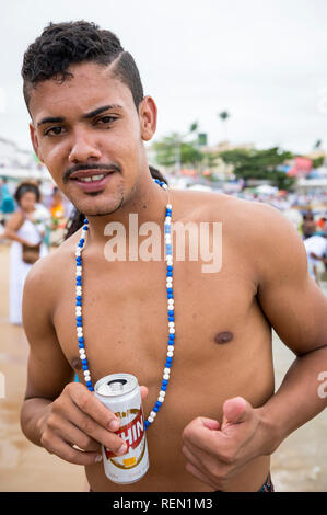 SALVADOR, BRÉSIL - février 02, 2016 : un jeune célébrant, vêtu d'un bleu et blanc traditionnel beaded necklace boit de la bière au Festival de Yemanja Banque D'Images