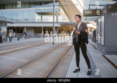 Jeune étudiant asiatique d'écouter de la musique à l'arrêt de tram Banque D'Images