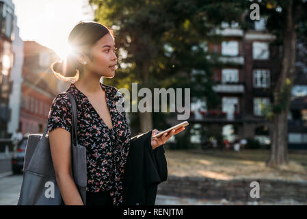Young Asian businesswoman standing outside après le travail à l'aide de son portable Banque D'Images