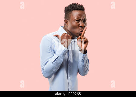 Secret, gossip concept. Jeune homme afro whispering a secret derrière sa main. Businessman isolé sur fond rose à la mode studio. Jeune homme émotif. Les émotions humaines, l'expression faciale concept. Banque D'Images
