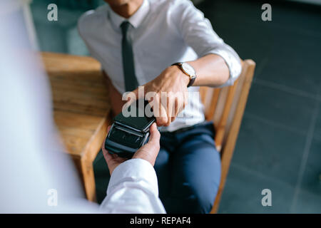 L'homme de loi de payer par téléphone mobile en utilisant la technologie NFC. De gros plan homme main tenant son téléphone sur un lecteur de carte de la machine pour faire le paiement Banque D'Images