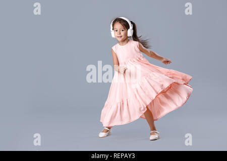 Petite fille en robe et casques d'écoute de la musique et des danses Banque D'Images
