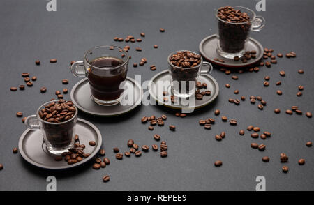 Coffee Time. Le café et les grains de café dans des tasses en verre avec sausers, sur fond de couleur noire Banque D'Images