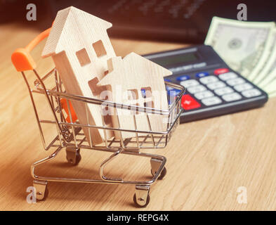 Maisons en bois dans un chariot de supermarché, d'argent et d'une calculatrice. L'analyse du marché immobilier. Concept immobilier. Vente et achat de biens. Louer Banque D'Images