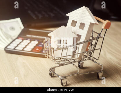 Maisons en bois dans un chariot de supermarché, d'argent et d'une calculatrice. L'analyse du marché immobilier. Concept immobilier. Vente et achat de biens. Louer Banque D'Images