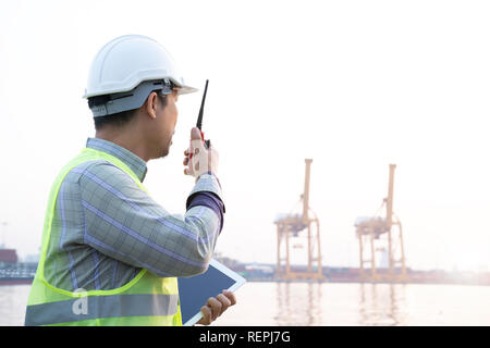 Ingénieur homme asiatique et radio tablet et travailler avec des conteneurs navire de fret en chantier pour Import Export logistique, l'arrière-plan de contrôle de sécurité. E Banque D'Images