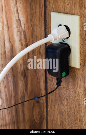 Close-up de cordon d'alimentation de l'ordinateur et d'un transformateur branché sur une prise de courant murale à l'intérieur d'une maison Banque D'Images