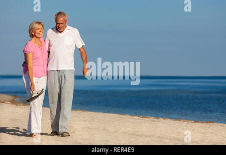 Happy senior man and woman couple walking laughing en vacances sur une plage tropicale déserte avec un ciel bleu clair et une mer calme Banque D'Images