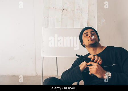 L'homme est agressif fume une cigarette et tenant un pistolet Banque D'Images