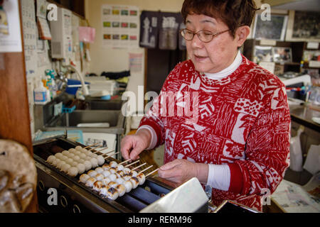 Une femme vu faire de riz japonais Sweet Dumpling Mitarashi dango "balle" dans inazawa, Mitarashi dango est la nourriture traditionnelle du Japon et il est très populaire, les boulettes sont enduits avec du soja et du sirop de sucre, et généralement de trois à cinq sont collés sur un bâton. Banque D'Images