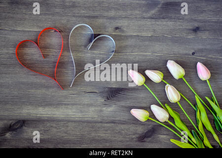 Deux coeurs de rouge et blanc avec des tulipes dans une douce nuance rose sur un fond de bois. Concept carte romantique. La vue du sommet. Mise à plat. Banque D'Images