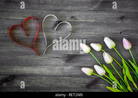 Deux coeurs de rouge et blanc avec des tulipes dans une douce nuance rose sur un fond de bois. Concept carte romantique. La vue du sommet. Mise à plat. Banque D'Images