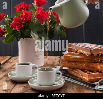 Gaufres Belges pour le petit-déjeuner pour deux. Des pâtisseries et un bouquet de roses rouges sur la table. Délicieux déjeuner romantique. Photo pour la Saint-Valentin Banque D'Images