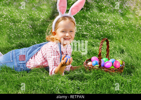 Happy little girl enfant la chasse les oeufs de Pâques dans le jardin. Banque D'Images