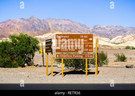 Posté indications routières et distances près du centre d'accueil de Furnace Creek, déserts et des montagnes en arrière-plan du paysage ; la vallée de la mort Nationa Banque D'Images