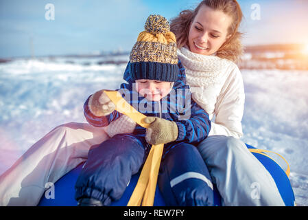 Jeune femme heureuse mère souriant, assis sur tube avec son fils garçon 3-6 ans, jouer à scrabing en hiver. Reste en hiver matin dans la nature. Banque D'Images