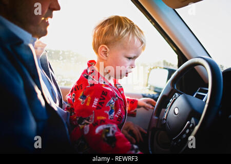 Petit garçon assis sur les genoux de son père dans la voiture du conducteur Banque D'Images